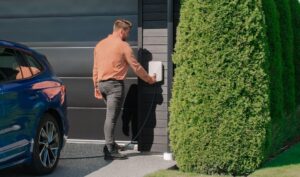 Man laddar sin blå elbil med en modern laddbox monterad på en garagevägg.