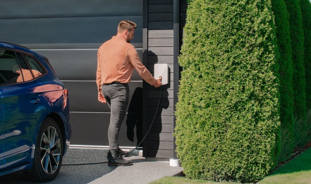 Man laddar sin blå elbil med en modern laddbox monterad på en garagevägg.