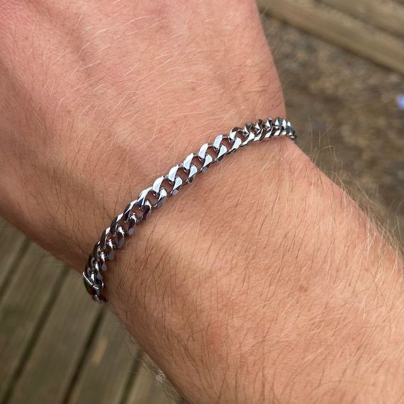 Ett tunt bismarck-liknande pansararmband i silver på en mans handled.