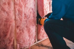 Person i skyddskläder arbetar med rosa isolering mellan träreglar
