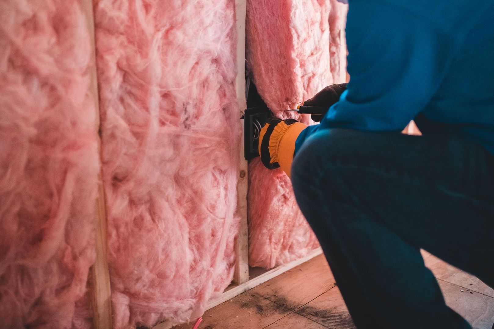 Person i skyddskläder arbetar med rosa isolering mellan träreglar